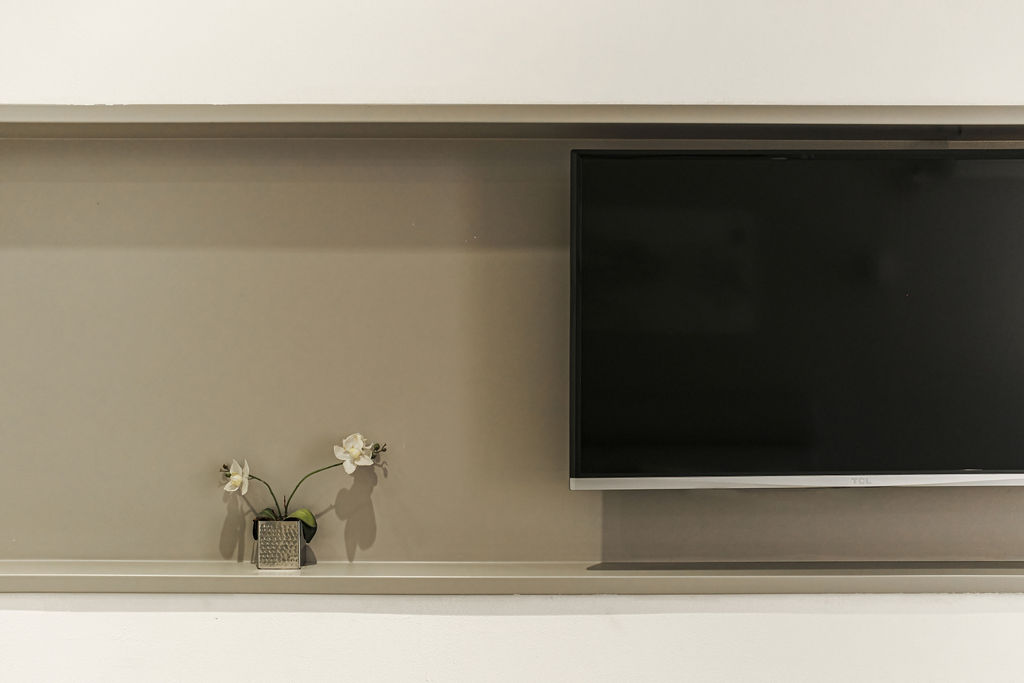 Téléviseur mural et orchidée sur étagère beige à l'Hotel Kikar Netanya