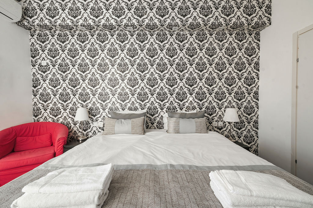 Chambre King avec papier peint damassé et fauteuil rouge à l'Hotel Kikar Netanya