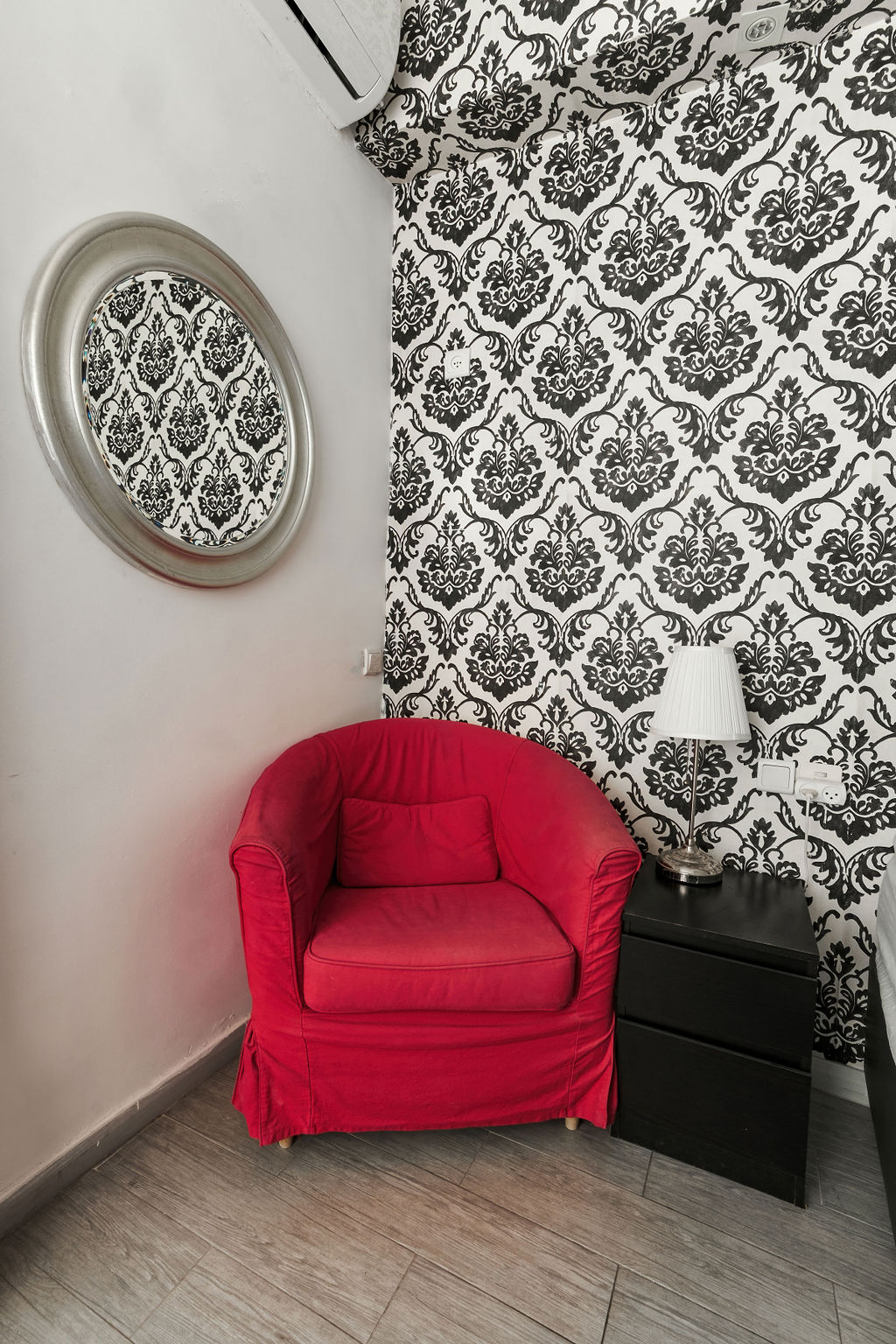 Fauteuil rouge et miroir rond argenté devant papier peint damassé