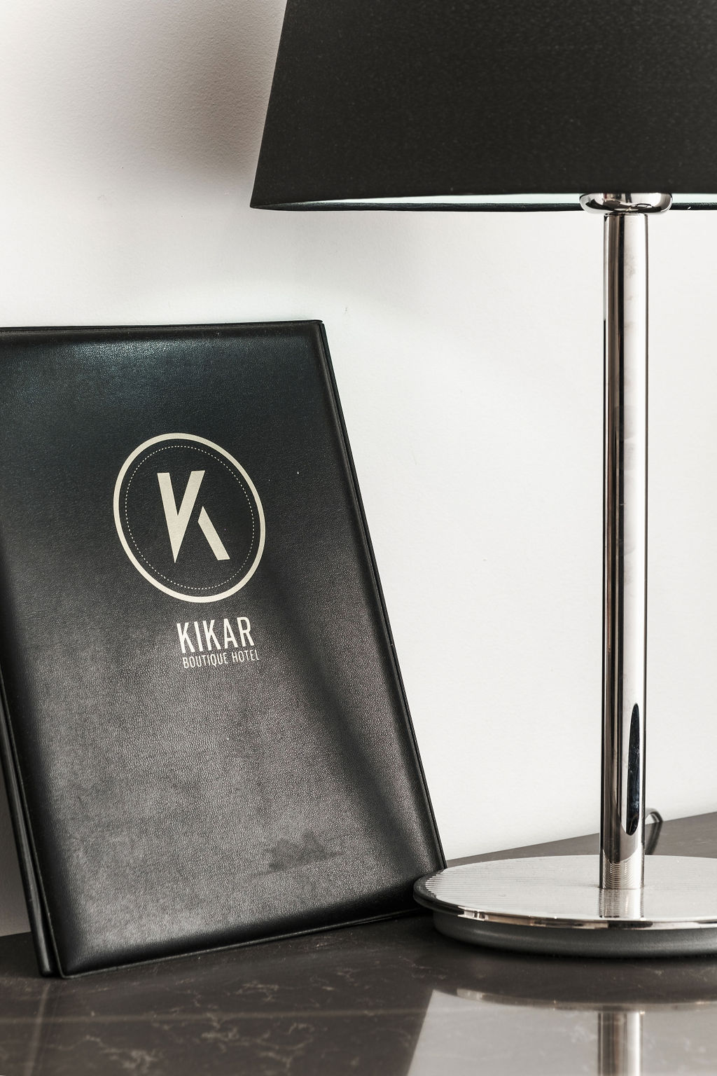 Menu en cuir Kikar Boutique Hotel posé près d'une lampe chromée